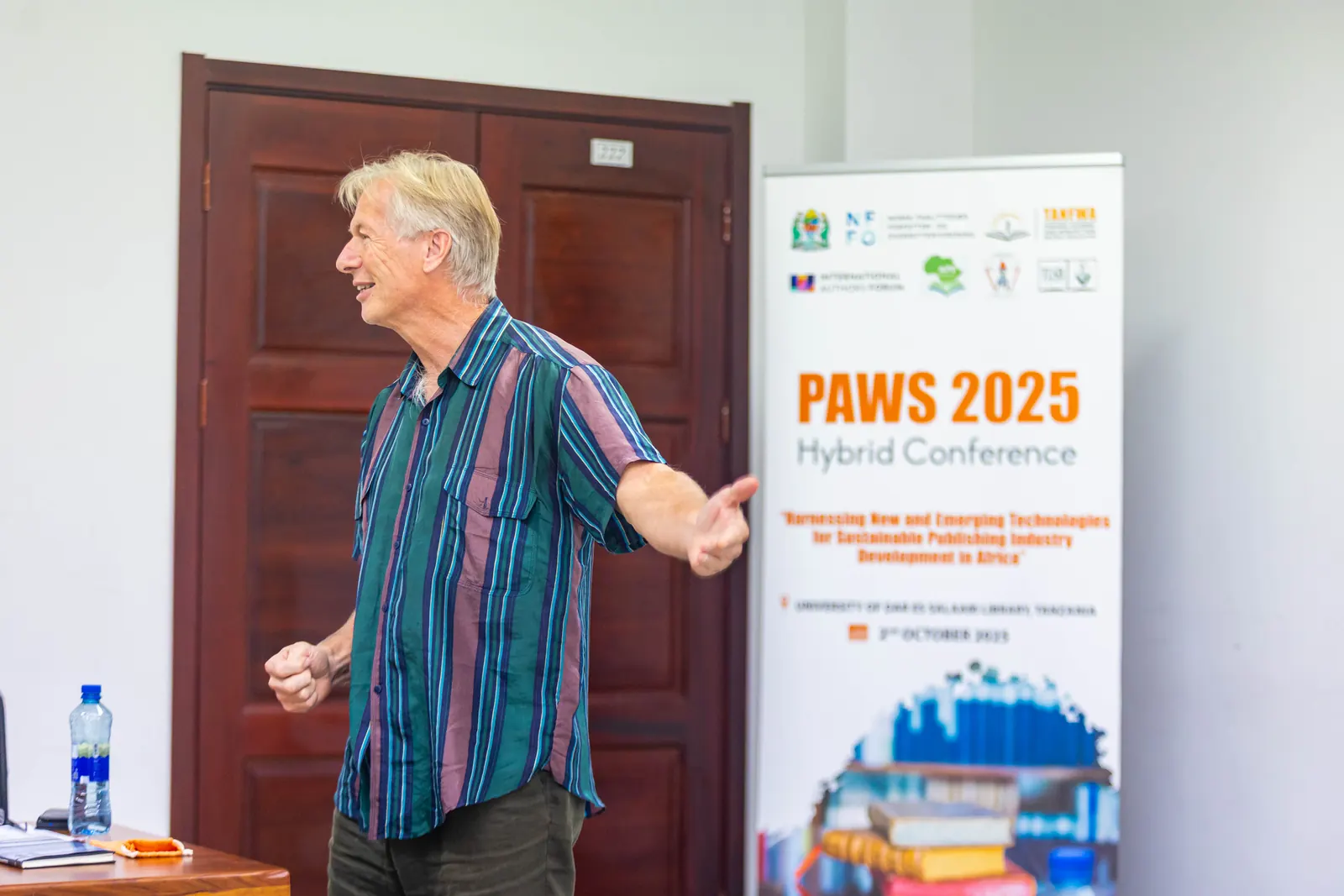 A keynote speaker addressing delegates beside the PAWS 2025 Hybrid Conference banner